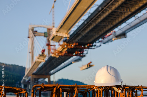White safety helmet on reinforcing bars with a bridge in construction in background. Construction site.