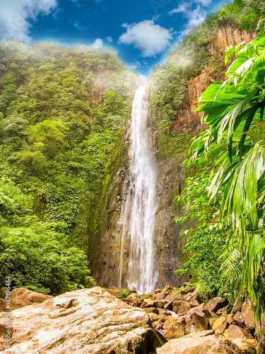Vertical shot of the colorful Carbet Falls or Les Chutes du Carbet in Basseterre, french tropical rainforest of Guadeloupe island on blue sky day, French Caribbean and greatest Guadeloupe attraction.