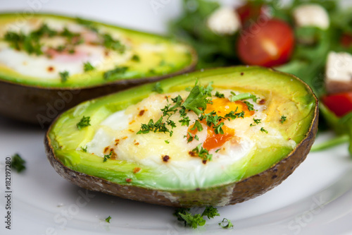 Roasted avocado with eggs sprinkled with parsley and salad with rocket salad, cherry tomatoes and feta cheese