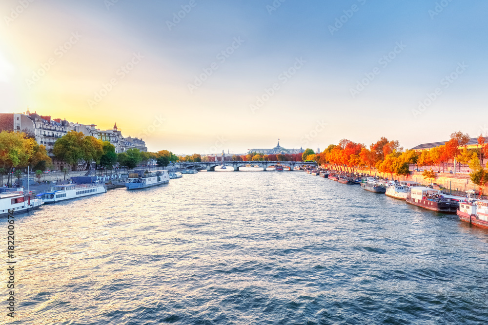 Obraz premium Paris, France. View on the city over Seine river. Autumn sunset scenery. Exhibition hall in Grand Palace (Palais) in background and yellow fall trees on river banks.