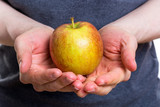 Holding an apple in both hands with a gray shirt on white background