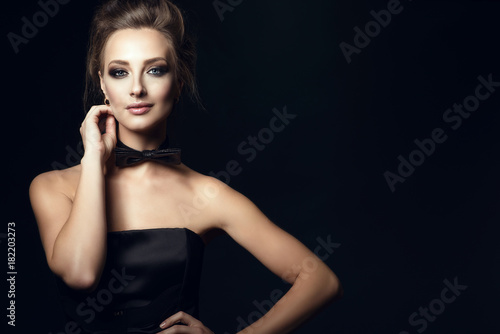 Closeup portrait of gorgeous glam woman with beautiful make up and updo hair wearing black corset dress and bow tie on her neck. Isolated on black background. Gamble and casino concept. Copy-space