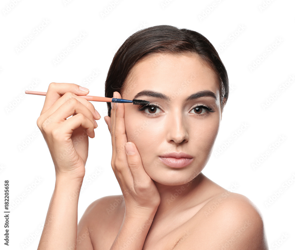 Beautiful young woman with eyelash extensions applying mascara, on white background