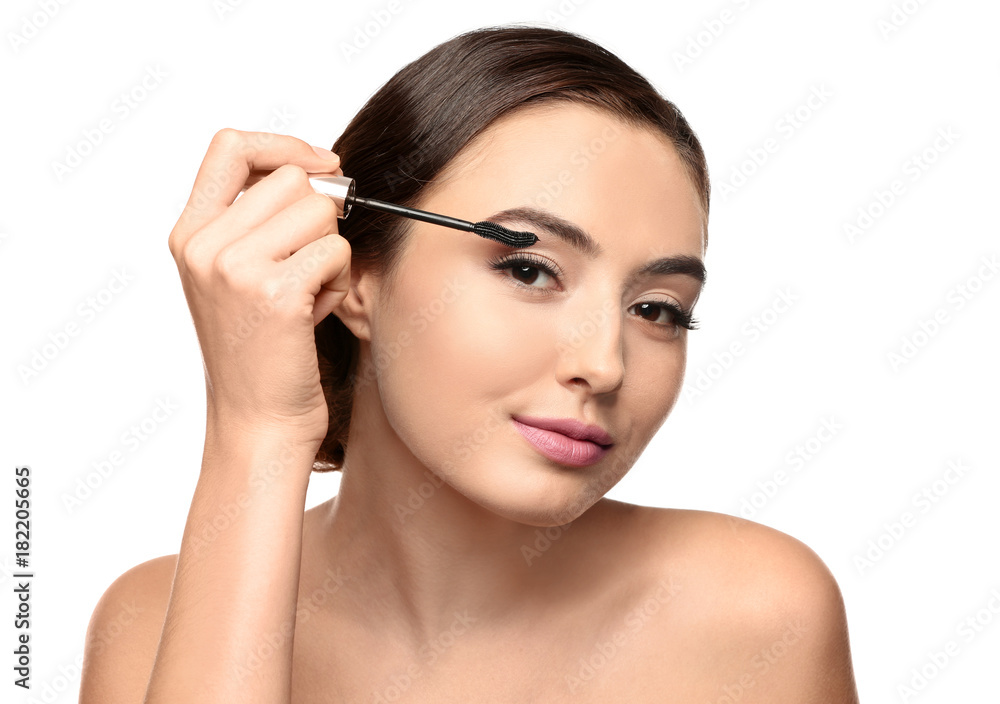 Beautiful young woman with eyelash extensions applying mascara, on white background Beautiful young woman with eyelash extensions applying mascara, on white background
