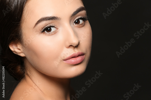 Beautiful young woman with eyelash extensions on dark background