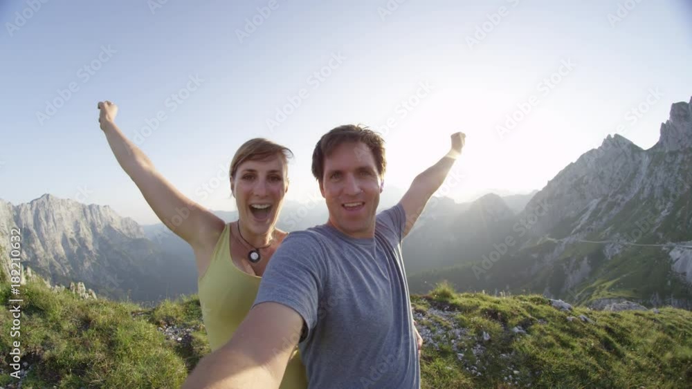 SELFIE PORTRAIT: Elated young couple taking selfie on mountaintop in summer. Cheerful hikers blowing off steam after a long hike. Victorious trekkers outstretching arms upon reaching mountain peak. SELFIE PORTRAIT: Elated young couple taking selfie on mountaintop in summer. Cheerful hikers blowing off steam after a long hike. Victorious trekkers outstretching arms upon reaching mountain peak.