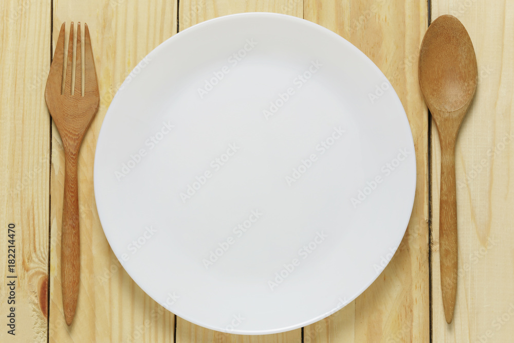 White plate and wooden spoon rests on a brown wood floor. White plate and wooden spoon rests on a brown wood floor.