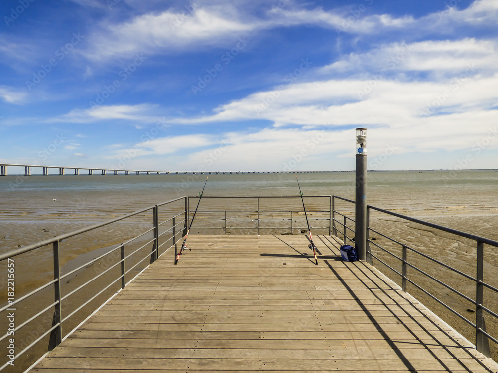 Fishing rods at a pier by the Tagus river at Parque das Nacoes - Vasco da Gama bridge in the background (Lisbon, Portugal)