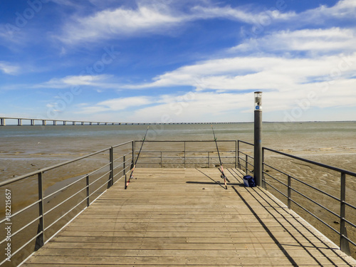 Fishing rods at a pier by the Tagus river at Parque das Nacoes - Vasco da Gama bridge in the background (Lisbon, Portugal)