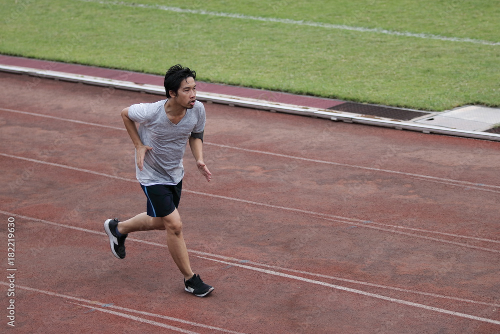 Handsome athlete Asian man running on racetrack in stadium with copy space background. Healthy active lifestyle concept. Handsome athlete Asian man running on racetrack in stadium with copy space background. Healthy active lifestyle concept.