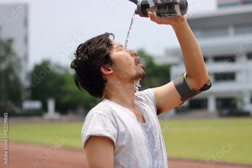Fototapeta Naklejka Na Ścianę i Meble -  Healthy young Asian runner pouring water with waterbottle on his face after running on track in stadium.