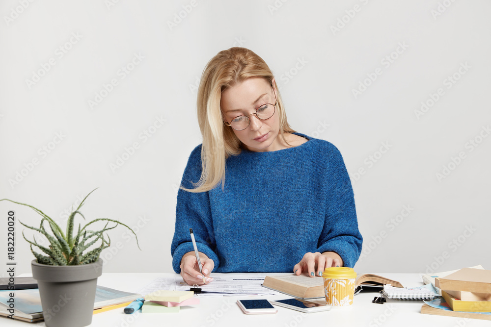 Serious concentrated female student or scientific worker rewrites information from book into notebook, tries to remember everything, prepares for presentation, involved in studying and preparation Serious concentrated female student or scientific worker rewrites information from book into notebook, tries to remember everything, prepares for presentation, involved in studying and preparation