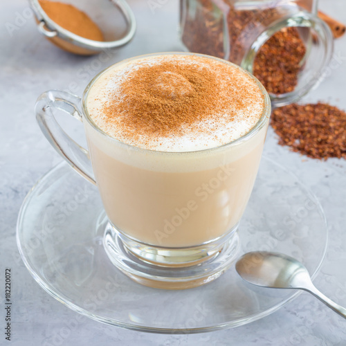 Healthy rooibos red tea latte topped with cinnamon, in a glass cup and ingredients on background, square