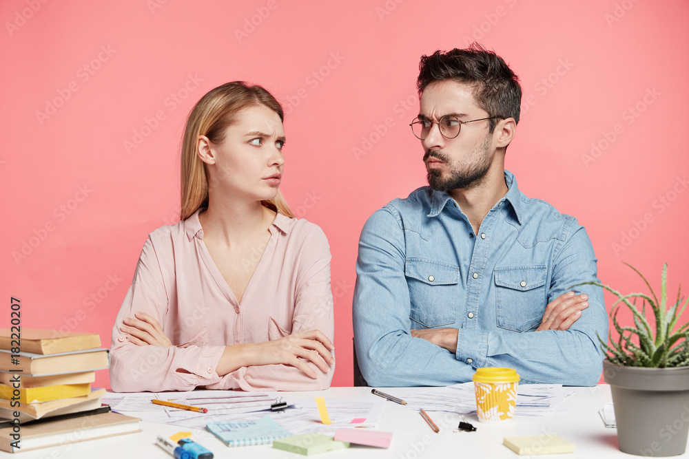 Two female and male students have disagreement, keep hands crossed, looks at each other angrily, can`t find common solution or decision. Professional coworkers quarrel during working process Two female and male students have disagreement, keep hands crossed, looks at each other angrily, can`t find common solution or decision. Professional coworkers quarrel during working process
