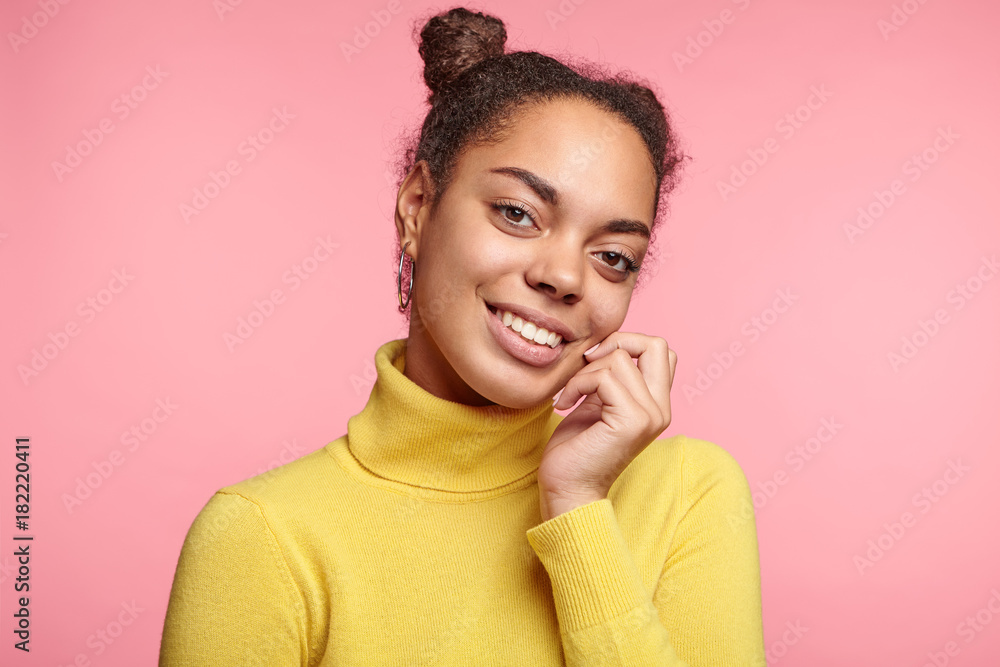 African American female model has two hair buns, dressed casually, looks with pleasant charming smile directly into camera, glad to pass exams or seminars successfully, rejoices coming winter holidays African American female model has two hair buns, dressed casually, looks with pleasant charming smile directly into camera, glad to pass exams or seminars successfully, rejoices coming winter holidays