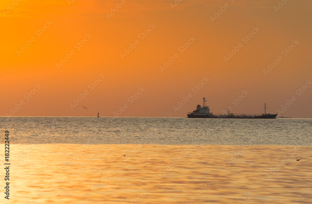 The evening sun with beautiful orange light and the cargo ship was running in the sea.