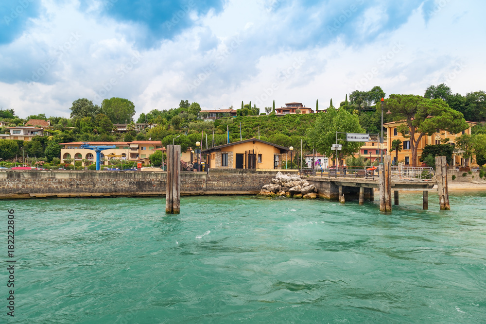 Small wooden pier city of Manerba del Garda is a quiet resort town on the Western shore of lake Garda. The view from the water on small Italian city.