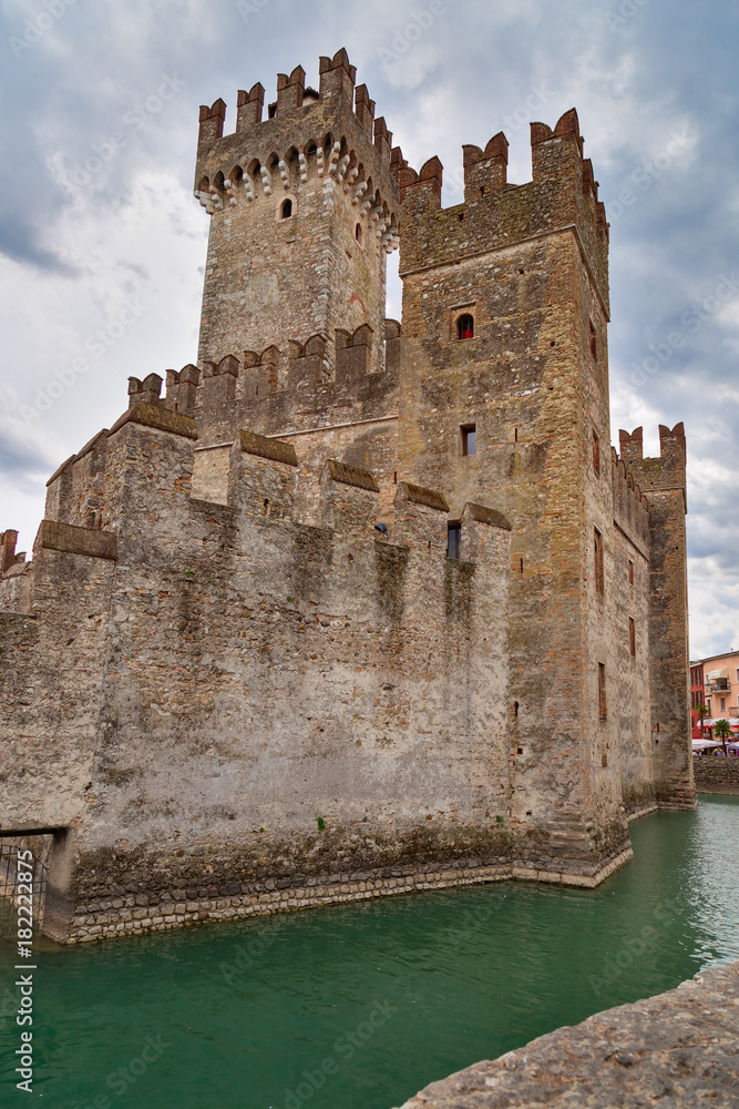 Scaliger castle is historical landmark of the city Sirmione in Italy on the lake Garda. Medieval Italian castle, wall of stone. Tall tower on a background of clouds.