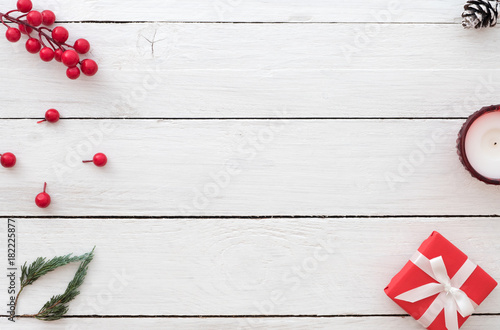 Christmas background with red gift box, holly berry, fir leaves, pine cone and candle on white wooden background. Creative Flat layout and top view design.