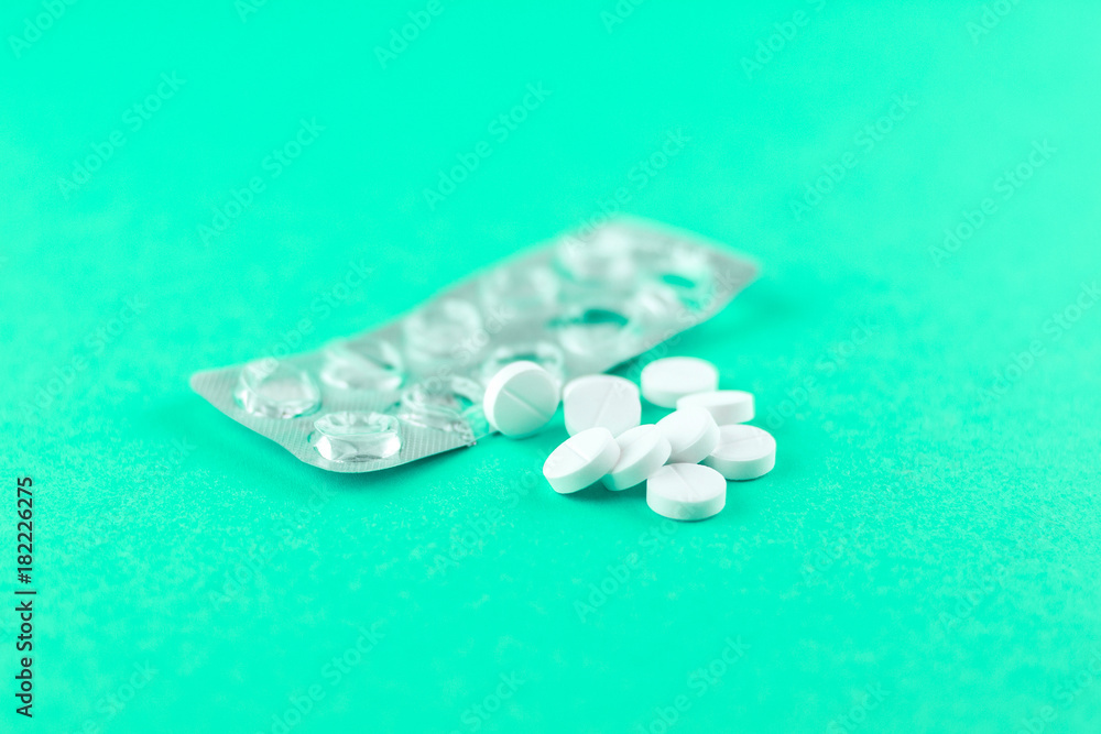 Empty pack with white pills packed in blister with copy space on aquamarine background. Focus on foreground, soft bokeh