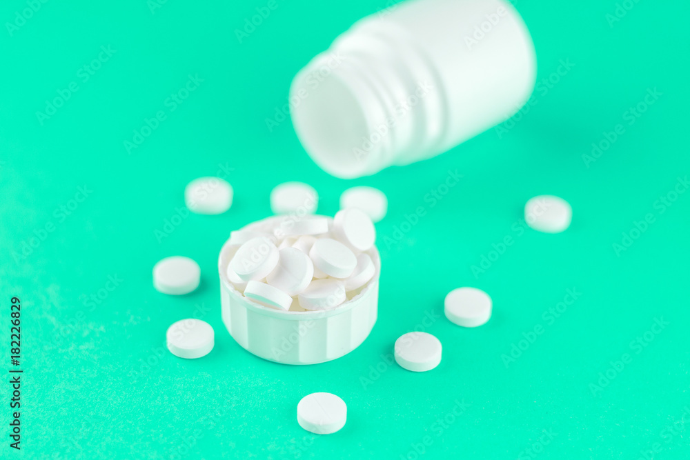 Close up white pill bottle with spilled out pills and capsules in cap on aquamarine background with copy space. Focus on foreground, soft bokeh. Pharmacy drugstore concept Close up white pill bottle with spilled out pills and capsules in cap on aquamarine background with copy space. Focus on foreground, soft bokeh. Pharmacy drugstore concept