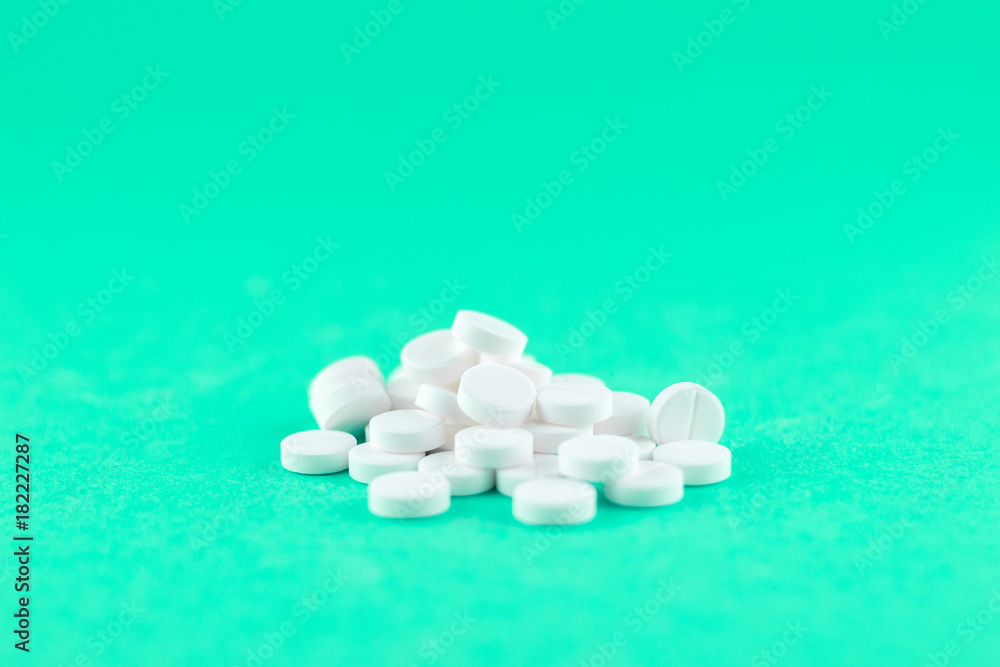 Close up white pills on aquamarine background with copy space. Focus on foreground, soft bokeh. Pharmacy drugstore concept