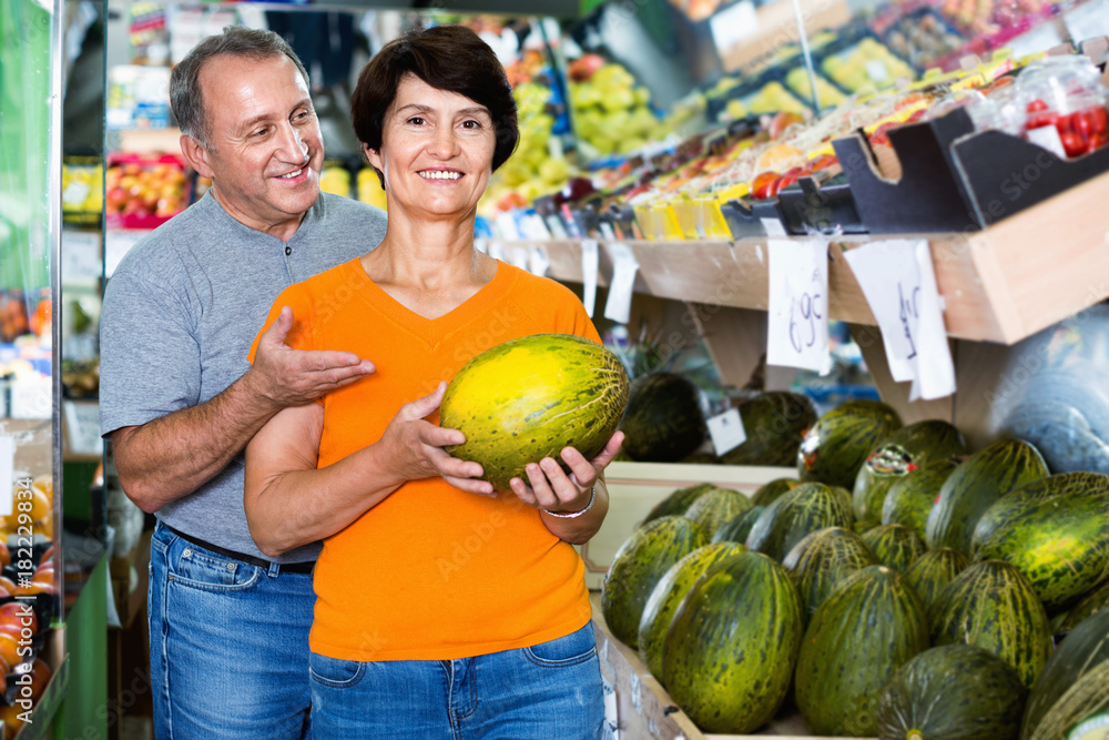 Fototapeta premium Smiling couple is choosing green melon in the supermarket.