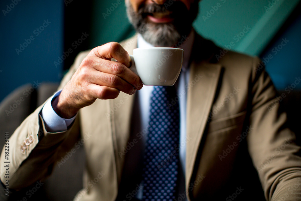 Handsome elegant serious businessman sitting in armchair and holding cup of espresso. Handsome elegant serious businessman sitting in armchair and holding cup of espresso.