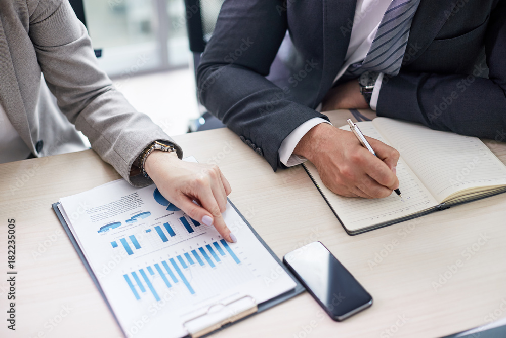 Close-up shot of unrecognizable colleagues studying financial figures while sitting at desk of modern open plan office Close-up shot of unrecognizable colleagues studying financial figures while sitting at desk of modern open plan office
