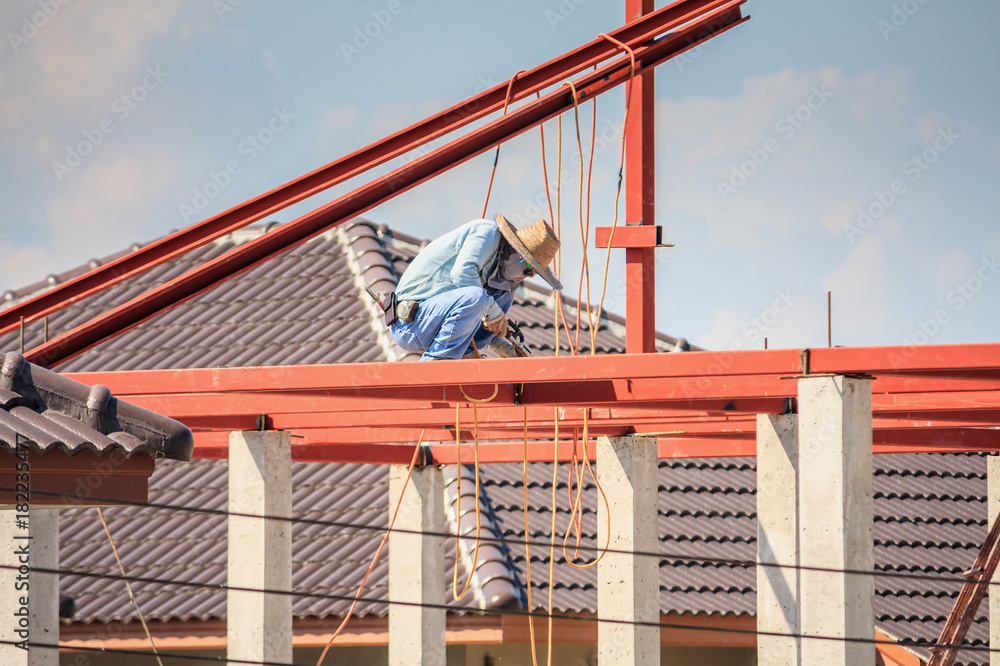 Naklejka premium welder workers installing steel frame structure of the house roof at building construction site