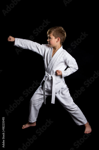 Clenched fist hit in karate. Serious kid in brand new kimono on isolated black background
