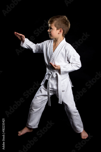 Full stance male fighter in kimono shows pose with open palms. Serious kid in brand new kimono on the black background
