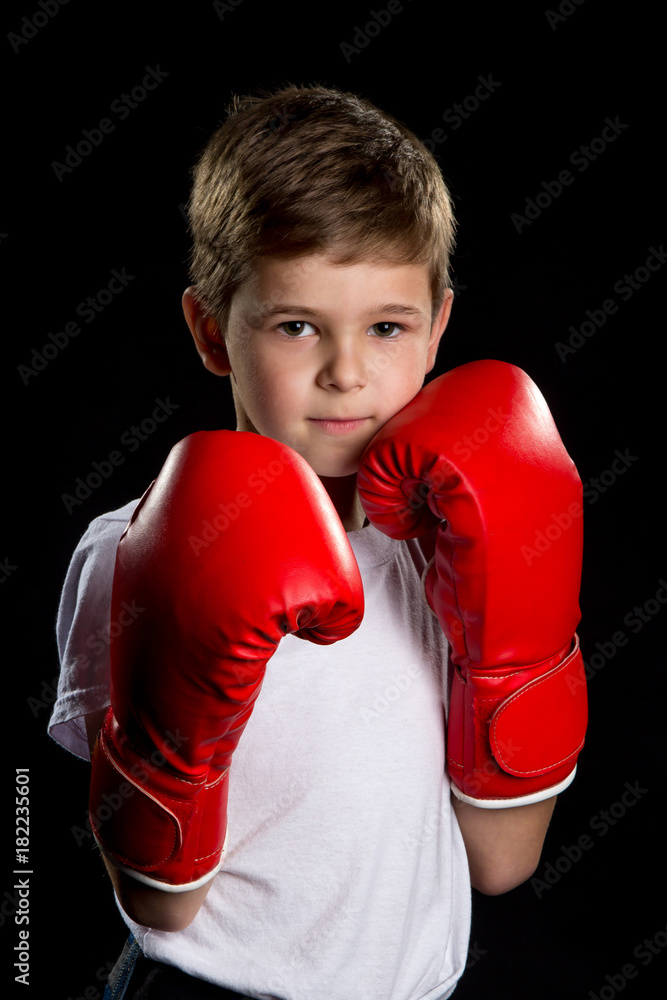 An angry, confident boxer with red gloves. Self defending position, boy portrait on the black background An angry, confident boxer with red gloves. Self defending position, boy portrait on the black background