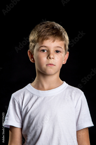 Thoughtful child portrait, intelligent boy on the black background looking straight