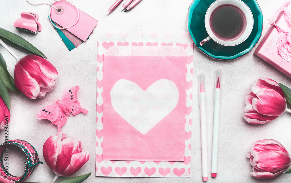 Pretty pink mock up with tulips, paper package with hearts, marker pen, tags and cup of coffee on creative desktop, top view, frame. Layout of spring greeting card for Mothers or Valentines day