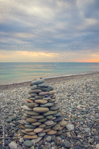 Fototapeta Naklejka Na Ścianę i Meble -  Zen stones stack on the beach with sea surf behind. Pebble tower and water waves with foam and splashes.Tranquility and disturbance concept. Sunny summer evening at Black sea coast.