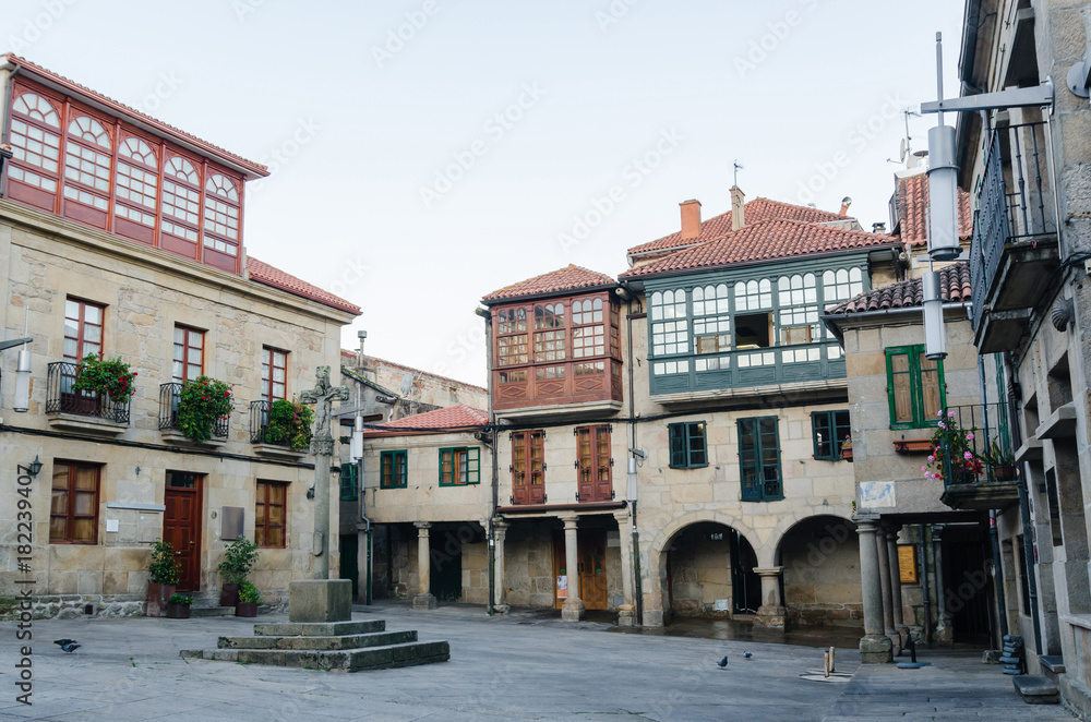 Historic square in Pontevedra. Buildings with coloured facade wooden windows balconies and a stone croos in the middle.