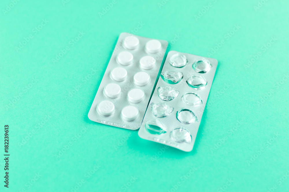 Full and empty packs of white pills packed in blisters with copy space on aquamarine background. Focus on foreground, soft bokeh Full and empty packs of white pills packed in blisters with copy space on aquamarine background. Focus on foreground, soft bokeh