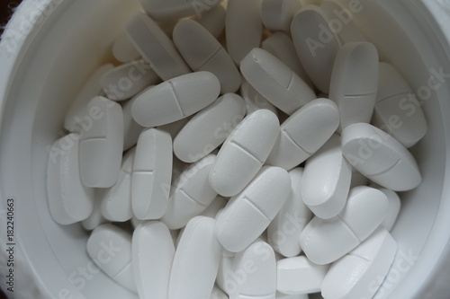 фотографія Plastic tub filled with white caplets from above