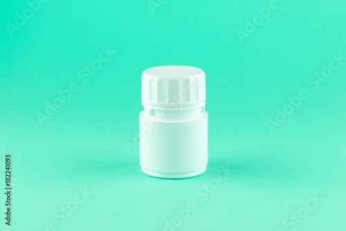 Close up white pill bottle on aquamarine background with copy space. Focus on foreground, soft bokeh. Pharmacy drugstore concept