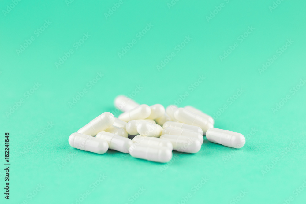 Close up white capsules on aquamarine background with copy space. Focus on foreground, soft bokeh. Pharmacy drugstore concept Close up white capsules on aquamarine background with copy space. Focus on foreground, soft bokeh. Pharmacy drugstore concept