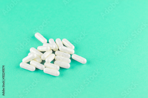 Close up white capsules on aquamarine background with copy space. Focus on foreground, soft bokeh. Pharmacy drugstore concept