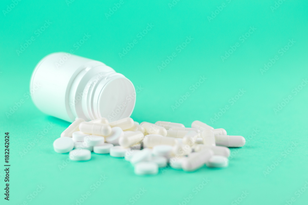 Close up white pill bottle with spilled out pills and capsules on aquamarine background with copy space. Focus on foreground, soft bokeh. Pharmacy drugstore concept Close up white pill bottle with spilled out pills and capsules on aquamarine background with copy space. Focus on foreground, soft bokeh. Pharmacy drugstore concept