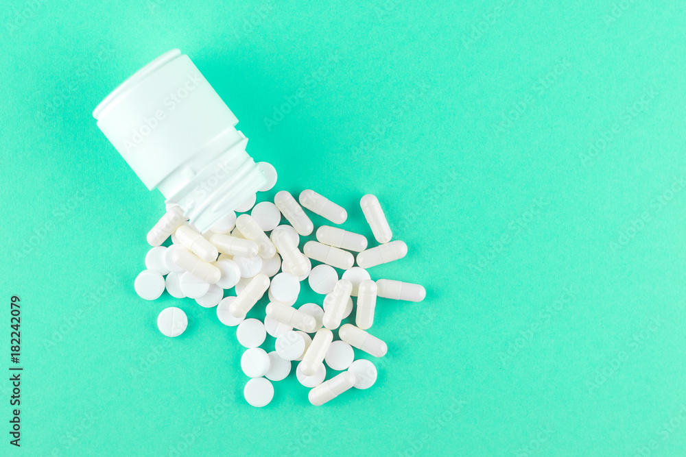 Close up white pill bottle with spilled out pills and capsules on aquamarine background with copy space. Focus on foreground, soft bokeh. Pharmacy drugstore concept. Top view Close up white pill bottle with spilled out pills and capsules on aquamarine background with copy space. Focus on foreground, soft bokeh. Pharmacy drugstore concept. Top view