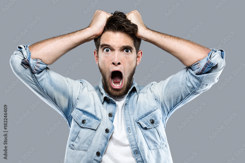 Angry young man screaming over gray background. Angry young man screaming over gray background.
