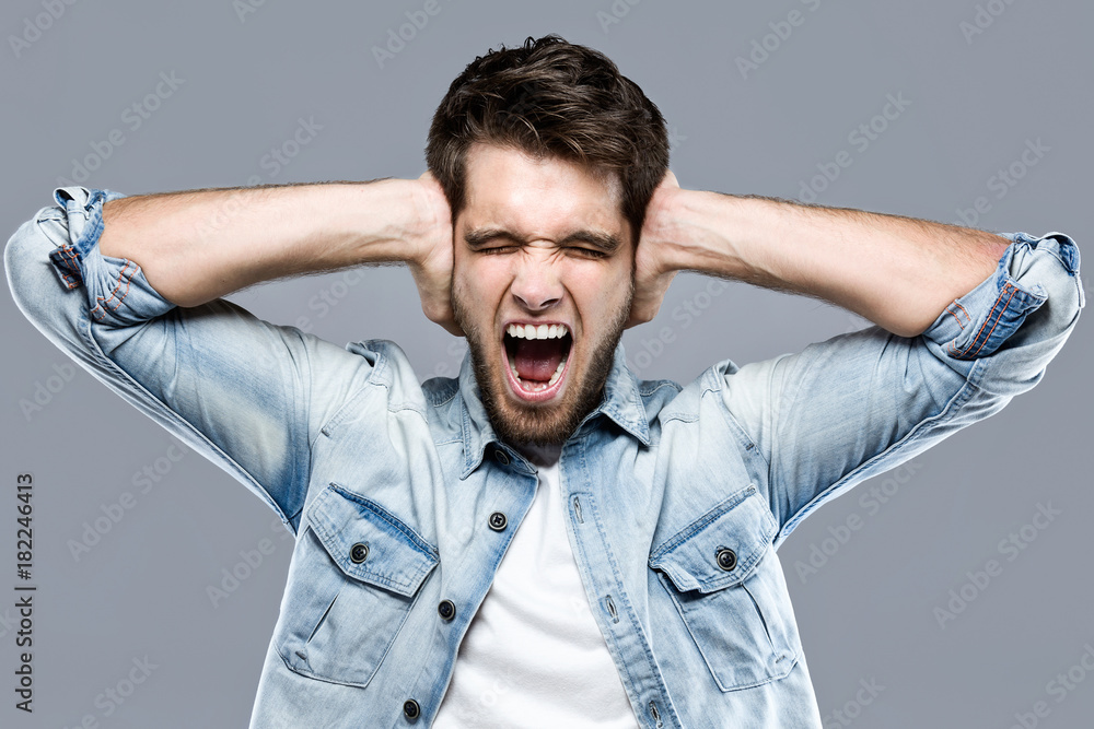 Handsome young man covering her ears over gray background. Handsome young man covering her ears over gray background.