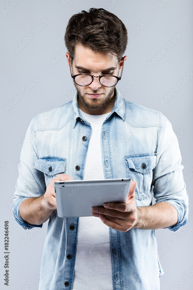 Handsome young man using his digital tablet over gray background. Handsome young man using his digital tablet over gray background.