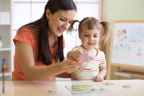 mother and daughter doing playing puzzle toy together on the table in children room photo