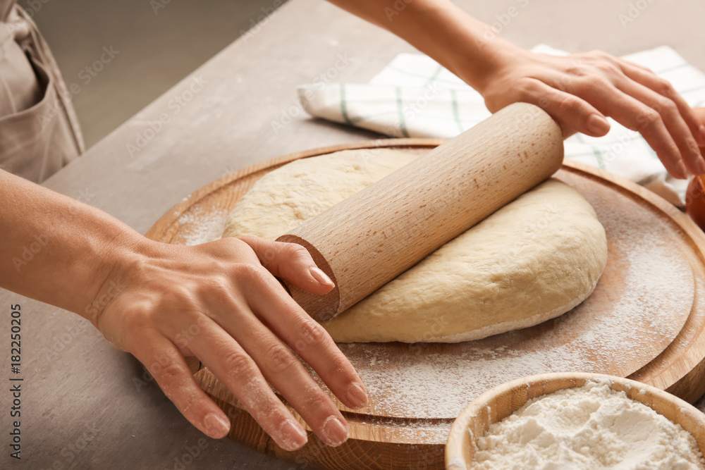 Female chef rolling dough on wooden board at kitchen Female chef rolling dough on wooden board at kitchen