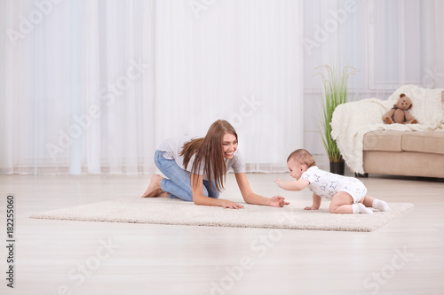 Young mother and cute baby playing on floor at home